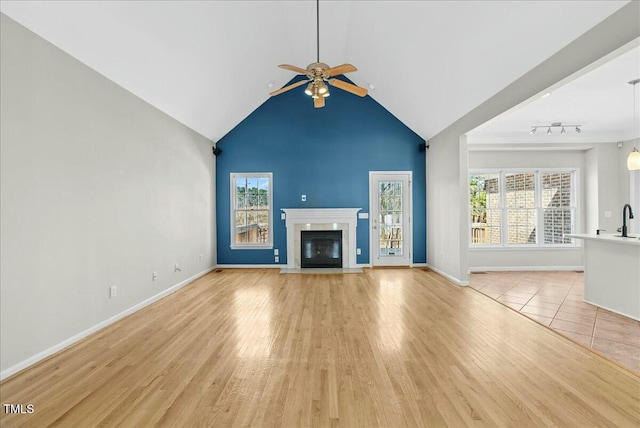 unfurnished living room with a fireplace with flush hearth, baseboards, light wood finished floors, and ceiling fan