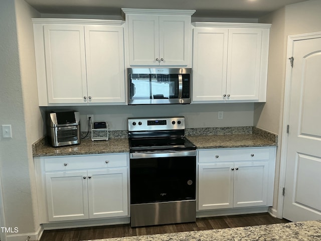 kitchen with dark wood-style floors, white cabinetry, stainless steel appliances, and dark stone counters