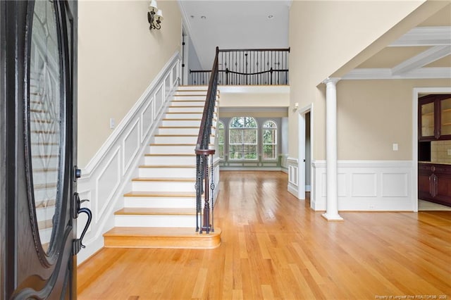 foyer entrance with a wainscoted wall, wood finished floors, a high ceiling, stairs, and ornate columns