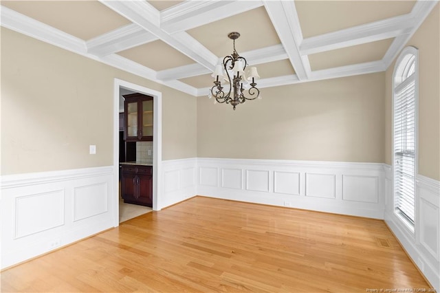 spare room featuring beam ceiling, coffered ceiling, an inviting chandelier, and light wood finished floors