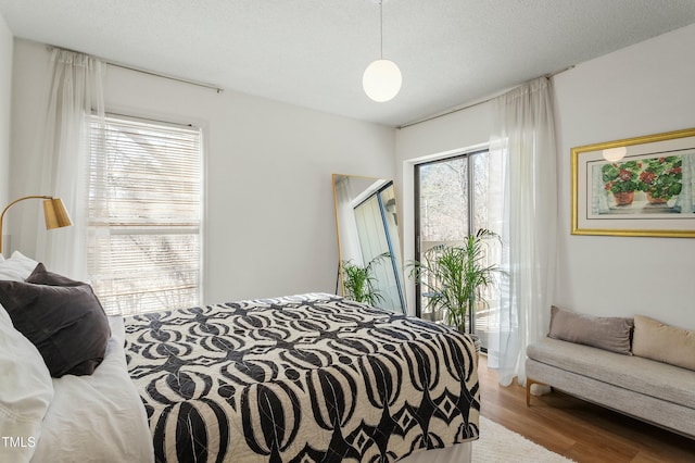 bedroom with access to outside, a textured ceiling, and wood finished floors