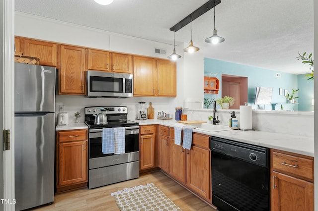 kitchen with visible vents, decorative light fixtures, light wood-style floors, stainless steel appliances, and a sink