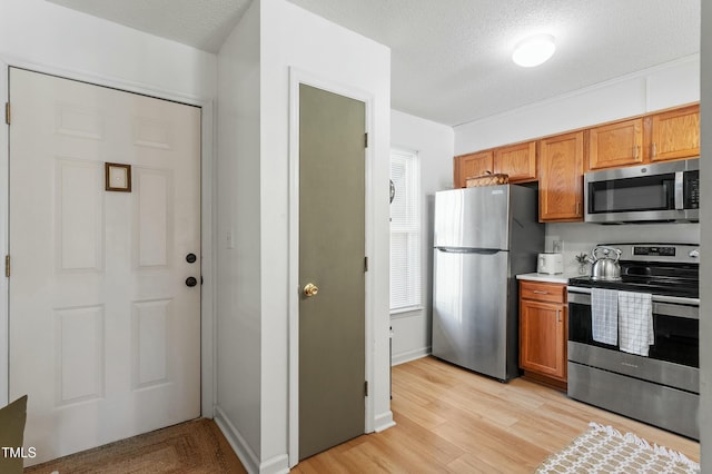 kitchen featuring stainless steel appliances, a textured ceiling, light countertops, and light wood finished floors