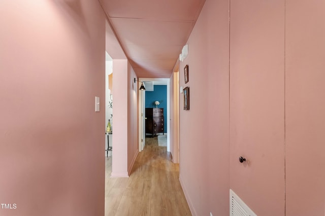 hall with visible vents, baseboards, and light wood-style flooring