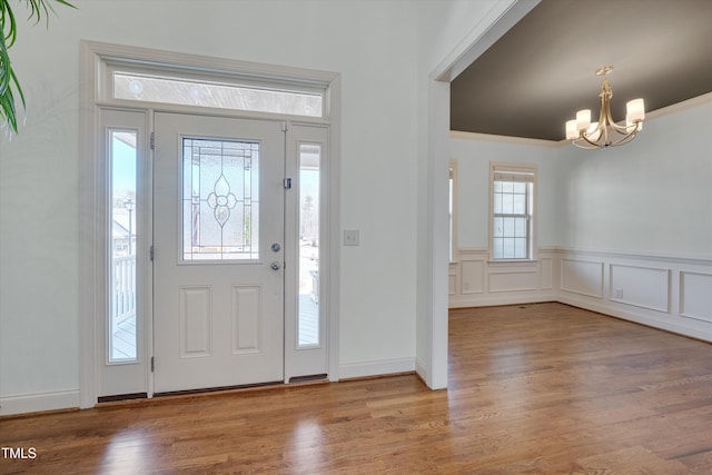 foyer with a decorative wall, wood finished floors, a wainscoted wall, and a chandelier