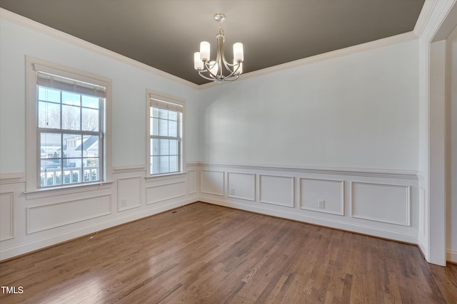 empty room featuring visible vents, crown molding, a wainscoted wall, wood finished floors, and a notable chandelier