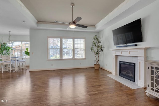 unfurnished living room with a fireplace with flush hearth, a raised ceiling, wood finished floors, and crown molding