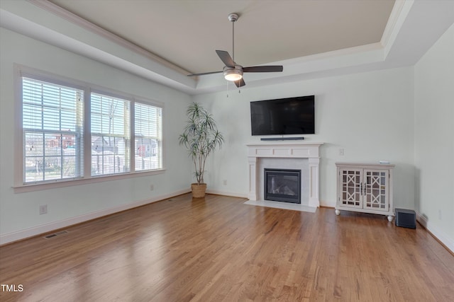 unfurnished living room with visible vents, a fireplace with flush hearth, wood finished floors, a raised ceiling, and ceiling fan