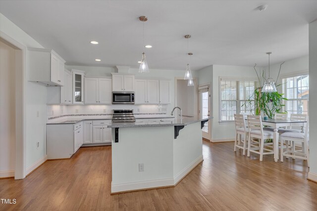 kitchen with light wood finished floors, glass insert cabinets, light stone countertops, stainless steel appliances, and white cabinetry