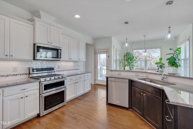 kitchen with light wood-style flooring, a sink, backsplash, white cabinetry, and stainless steel appliances