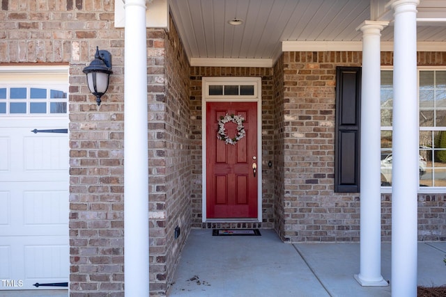 entrance to property featuring a porch, a garage, and brick siding