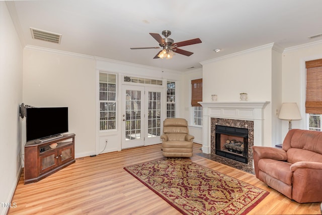 living room featuring a ceiling fan, visible vents, a high end fireplace, light wood-style floors, and crown molding