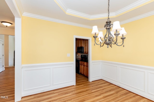 unfurnished dining area featuring a wainscoted wall, a chandelier, ornamental molding, and light wood finished floors