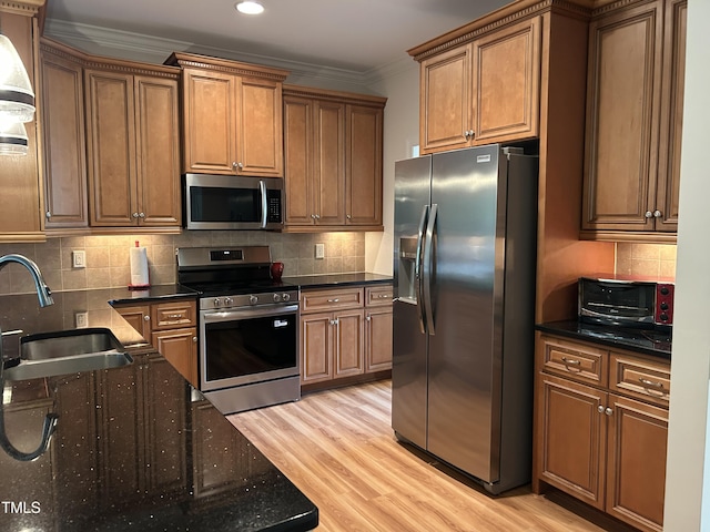kitchen with light wood finished floors, a sink, stainless steel appliances, crown molding, and backsplash