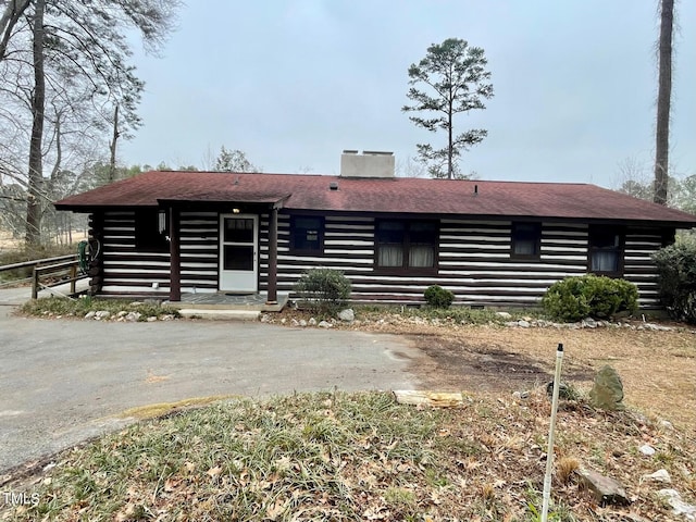 log-style house with driveway, log exterior, a chimney, and a shingled roof