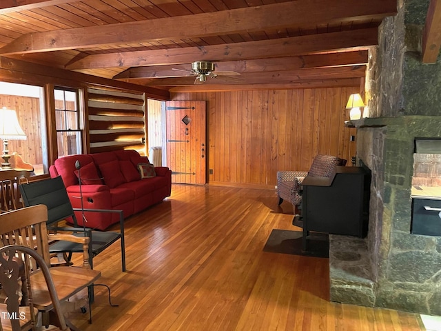 living room featuring beam ceiling, a stone fireplace, wood ceiling, wood walls, and wood-type flooring