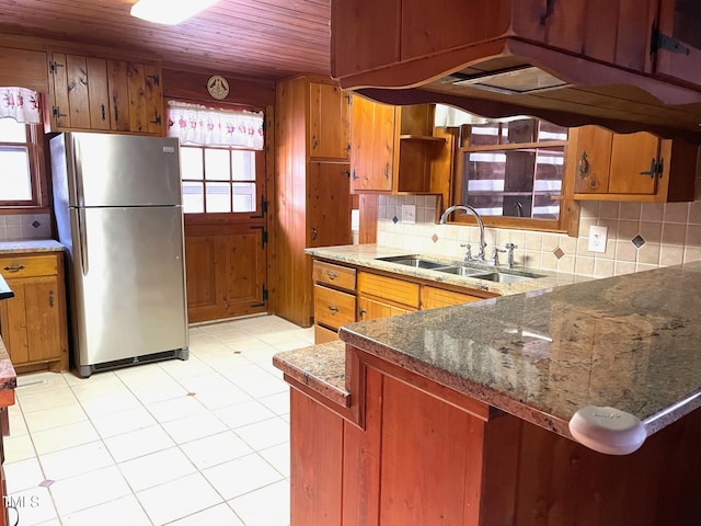 kitchen with a sink, decorative backsplash, brown cabinets, and freestanding refrigerator