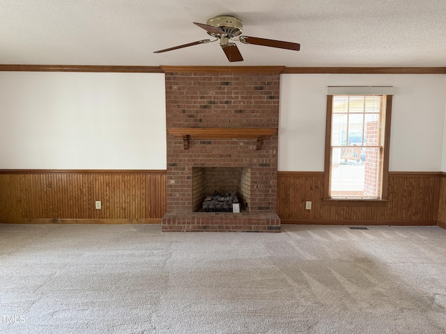 unfurnished living room featuring a textured ceiling, wooden walls, wainscoting, crown molding, and ceiling fan