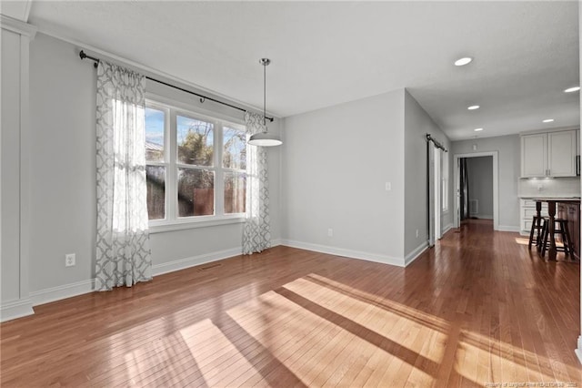 unfurnished dining area featuring recessed lighting, a barn door, baseboards, and hardwood / wood-style flooring