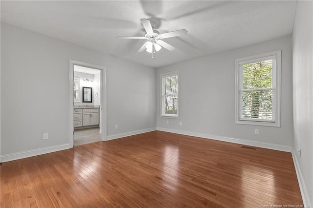 unfurnished bedroom with visible vents, connected bathroom, baseboards, a textured ceiling, and wood-type flooring