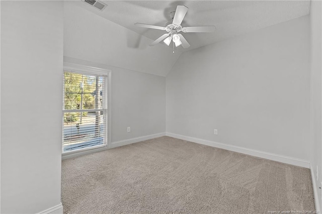 carpeted spare room with visible vents, ceiling fan, baseboards, and vaulted ceiling