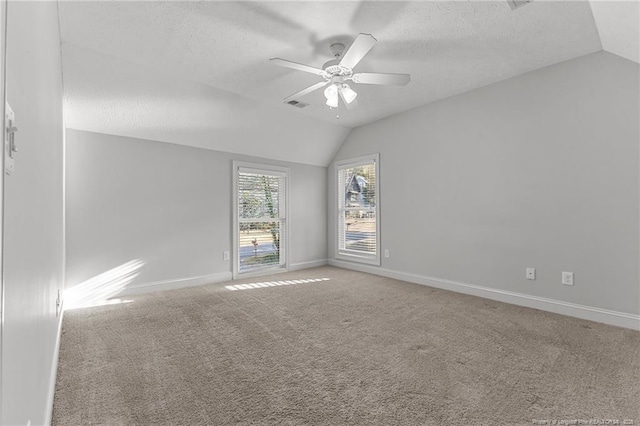 empty room featuring visible vents, a ceiling fan, a textured ceiling, carpet flooring, and vaulted ceiling