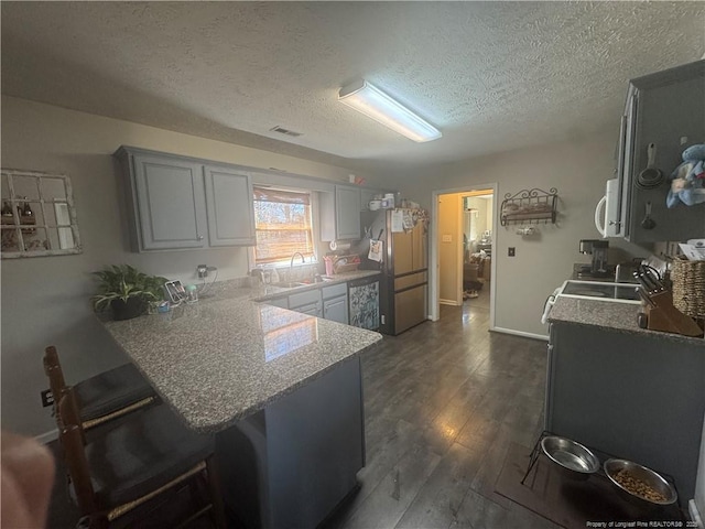 kitchen featuring visible vents, dark wood finished floors, a peninsula, freestanding refrigerator, and a kitchen bar