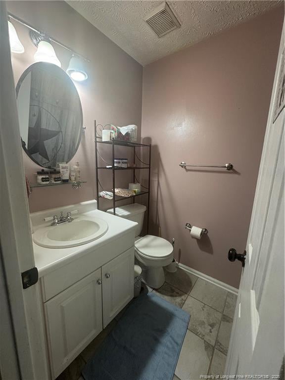 half bath with vanity, baseboards, visible vents, a textured ceiling, and toilet