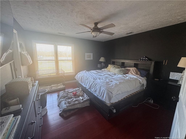 bedroom with a ceiling fan, baseboards, wood finished floors, visible vents, and a textured ceiling