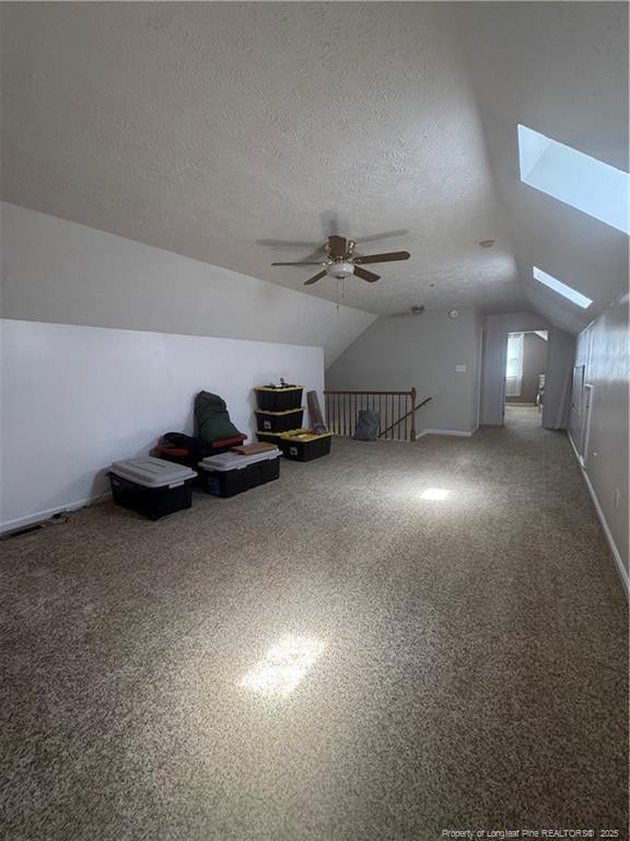 additional living space featuring lofted ceiling with skylight, a ceiling fan, baseboards, and a textured ceiling