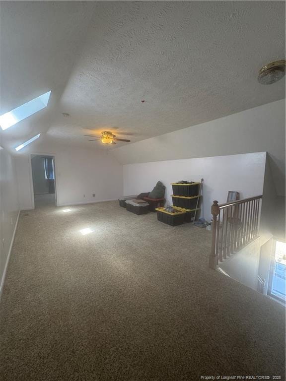 additional living space featuring lofted ceiling with skylight, a textured ceiling, and carpet