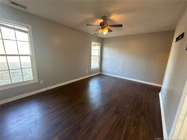 spare room with dark wood-style floors, visible vents, and baseboards