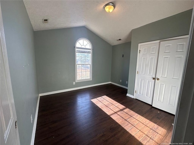 unfurnished bedroom featuring baseboards, visible vents, dark wood finished floors, vaulted ceiling, and a textured ceiling