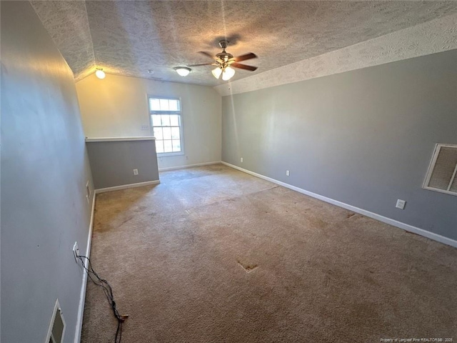 carpeted spare room featuring lofted ceiling, visible vents, baseboards, and a textured ceiling