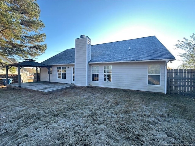 back of house featuring a lawn, fence, a gazebo, a shingled roof, and a chimney