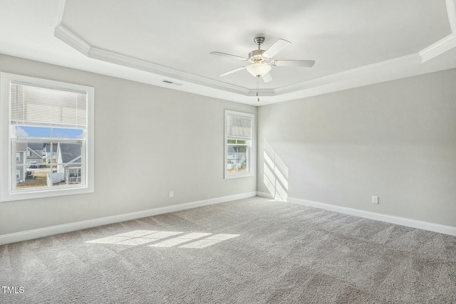 carpeted empty room with a tray ceiling, a ceiling fan, visible vents, and baseboards