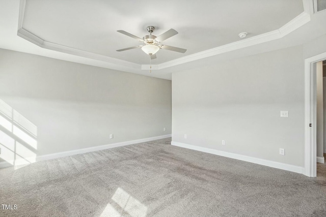 carpeted empty room featuring a tray ceiling, baseboards, ornamental molding, and a ceiling fan