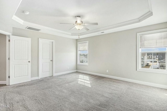 unfurnished bedroom featuring a tray ceiling, carpet flooring, baseboards, and visible vents