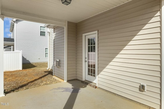 view of exterior entry featuring a patio and fence