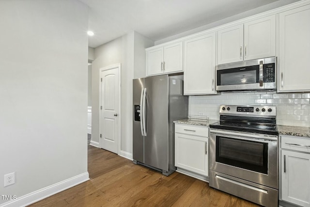 kitchen with light stone countertops, dark wood-style flooring, stainless steel appliances, white cabinetry, and tasteful backsplash