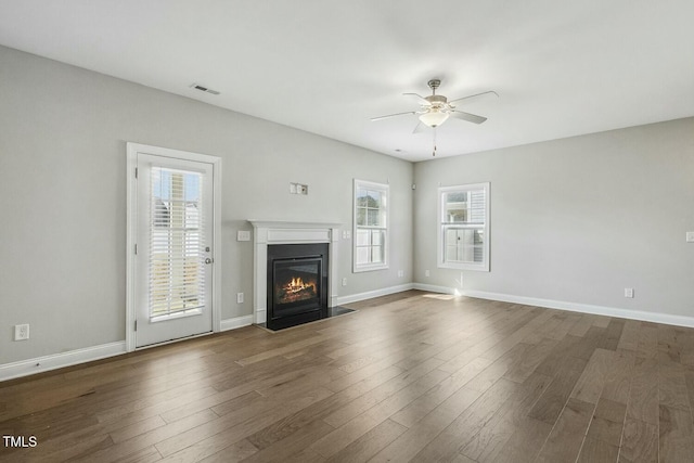 unfurnished living room with visible vents, a fireplace with flush hearth, ceiling fan, and dark wood-style flooring