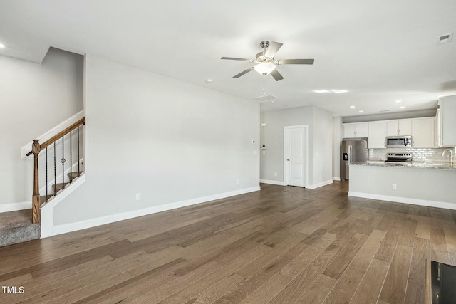 unfurnished living room with baseboards, stairs, ceiling fan, and dark wood-style flooring