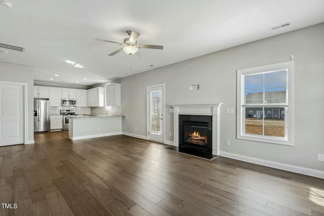 unfurnished living room featuring visible vents, baseboards, dark wood-style flooring, and a ceiling fan