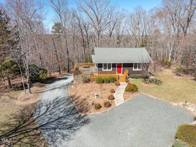 view of front facade with gravel driveway, a front yard, a deck, and a wooded view