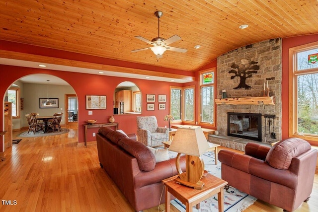 living area featuring a stone fireplace, wooden ceiling, light wood-style flooring, and arched walkways