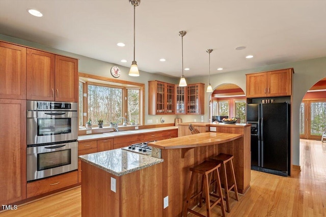 kitchen with a center island, light wood-type flooring, arched walkways, stainless steel appliances, and a sink