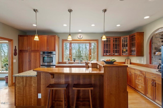 kitchen featuring oven, light wood-type flooring, a kitchen bar, a sink, and brown cabinetry