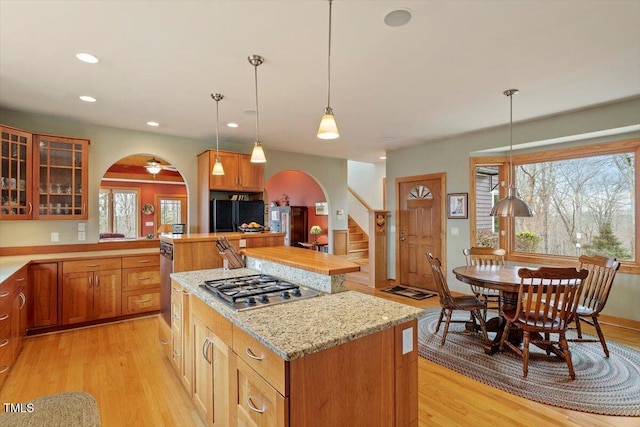 kitchen featuring stainless steel gas cooktop, light wood-style flooring, arched walkways, glass insert cabinets, and a center island