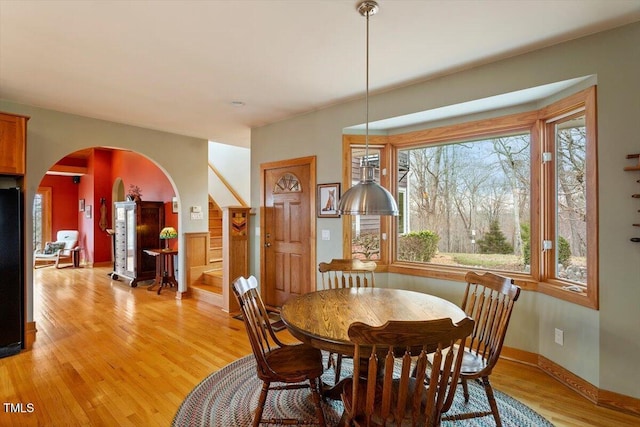 dining room with stairs, baseboards, arched walkways, and light wood finished floors