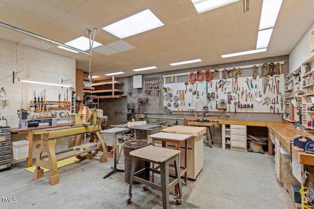 misc room with a drop ceiling, a workshop area, and concrete flooring